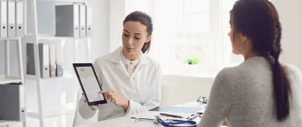 A doctor shows a patient a digital tablet with mental health care information in a bright office setting.