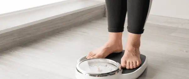 Person standing on a mechanical bathroom scale, tracking their weight loss journey, placed on a wooden floor.